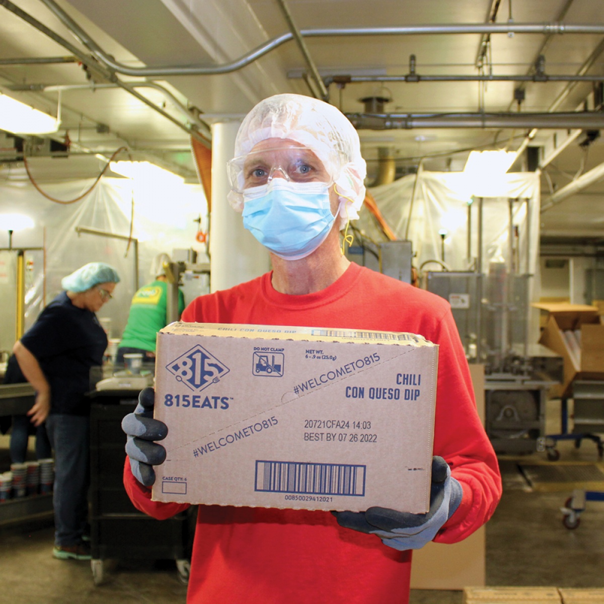 Photo of a worker in a hairnet and mask holding a box with 815Eats graphics